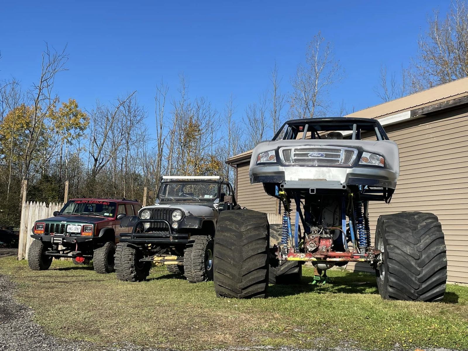 Two Jeeps and a lifted pickup on big tires parked beside the shop building