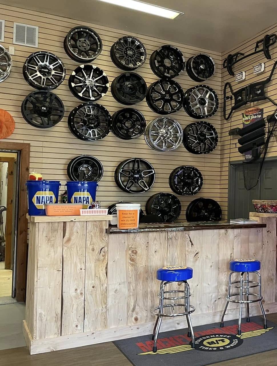 Wall of aftermarket wheels above a wooden service counter with two blue stools